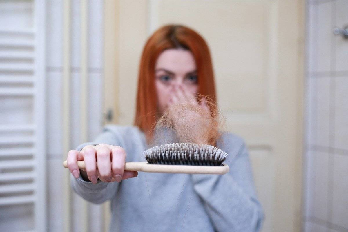 A woman holds out a brush with a lot of hair on it.