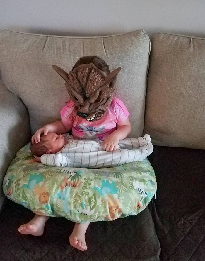Kid holding baby sibling while wearing a scary werewolf mask