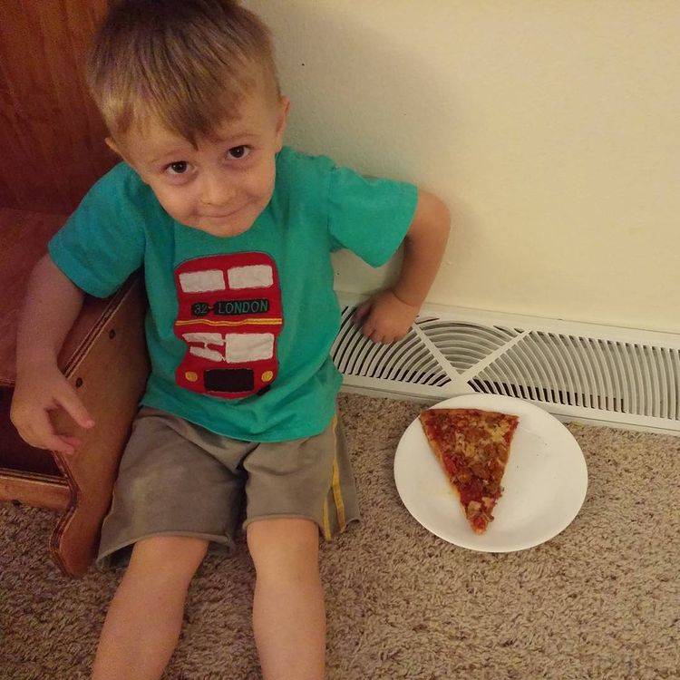 kid sitting beside air vent with slice of pizza