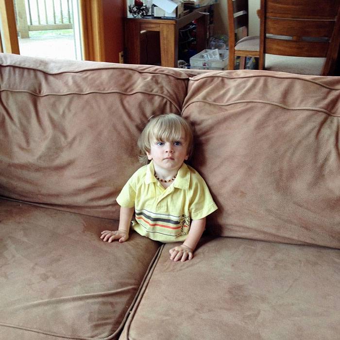 Kid sitting on couch with legs under the seat cushions