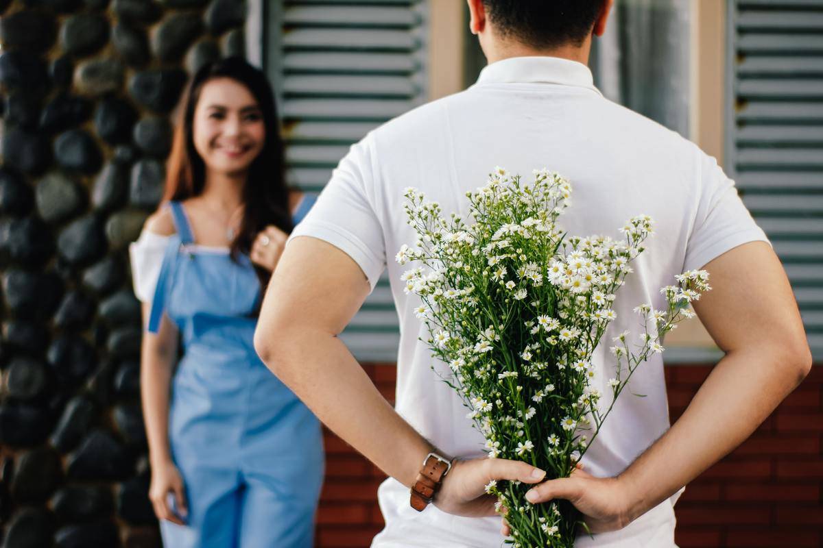 man holds flowers for girl behind his back