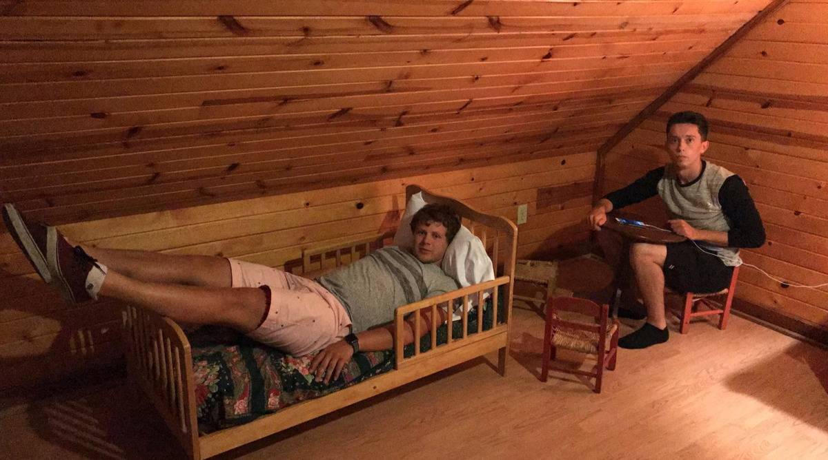 two men sitting in tiny bed and at tiny chair and table