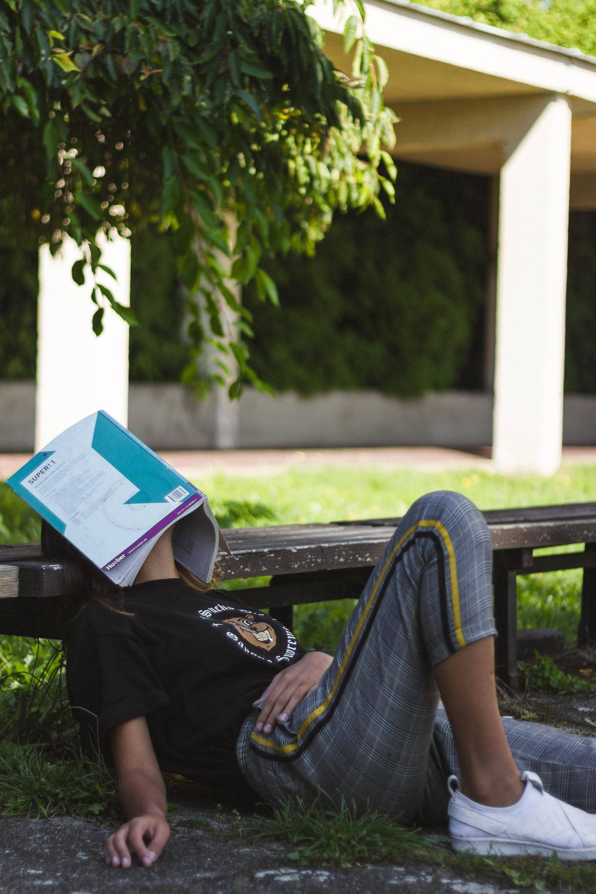 A woman sleeps outside with her book over her eyes. 