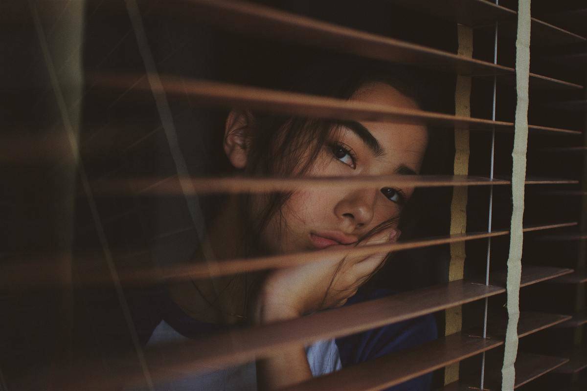 woman looking through window from the open blinds