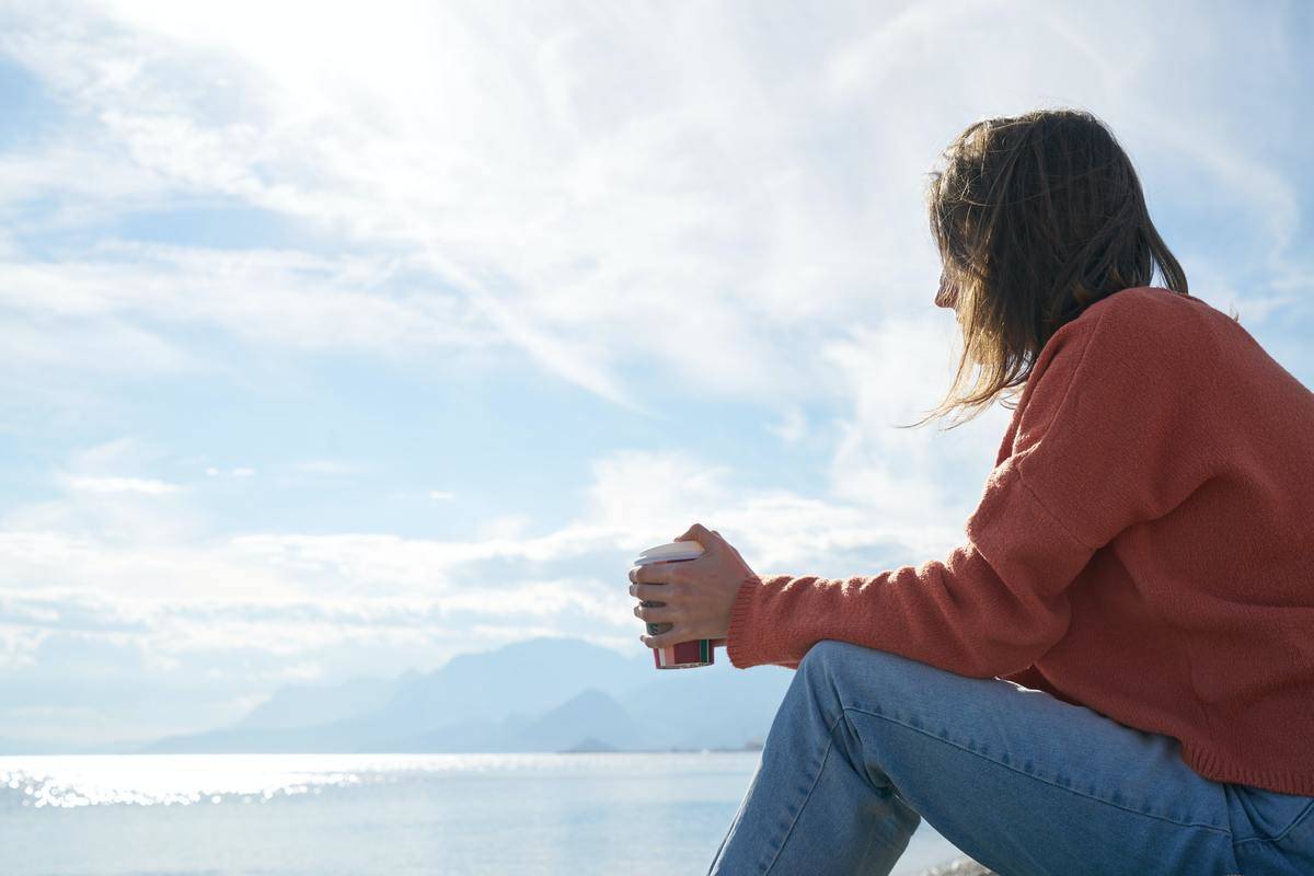 woman sips coffee by the water as she sits