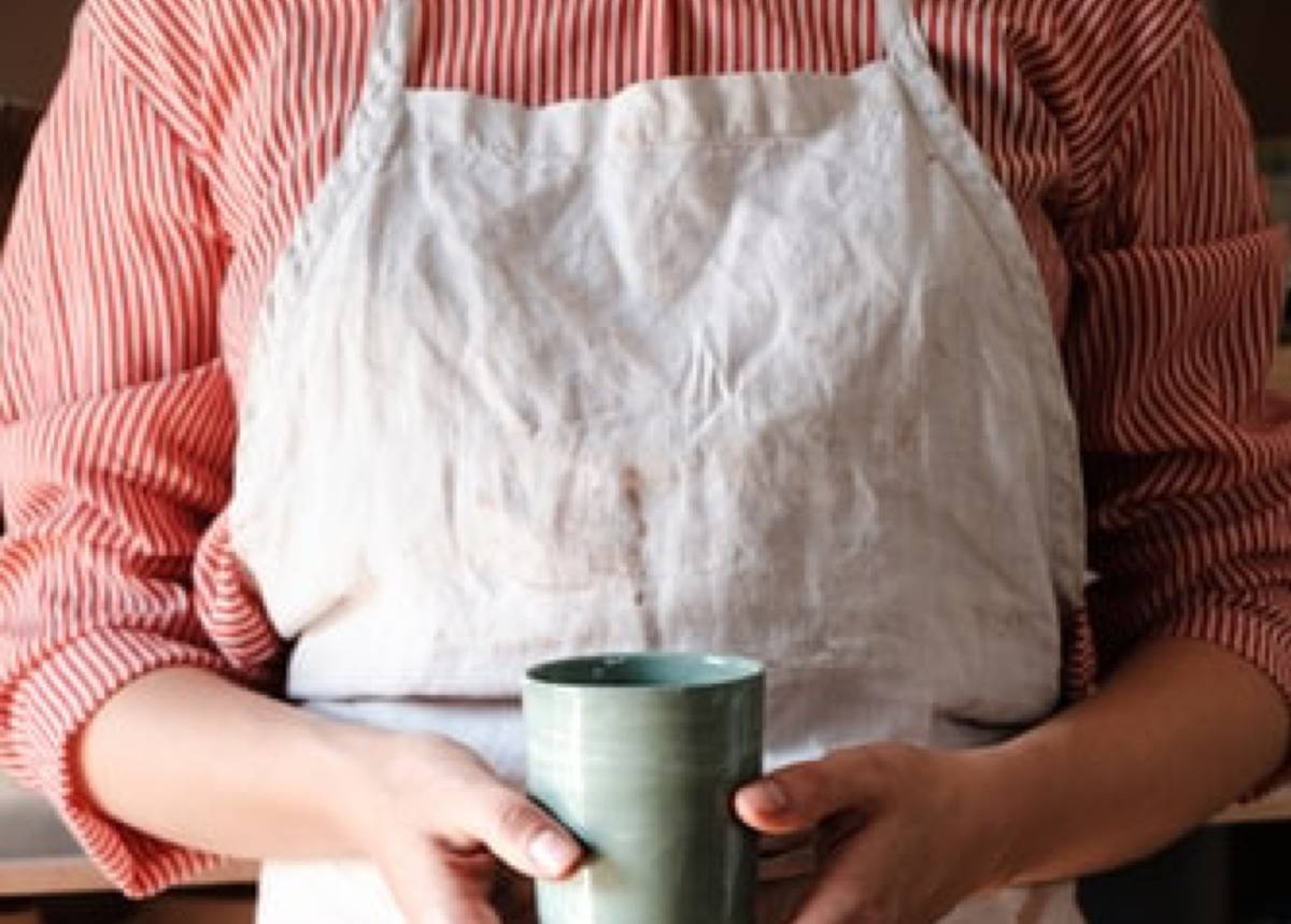 person in apron holding ceramic cup