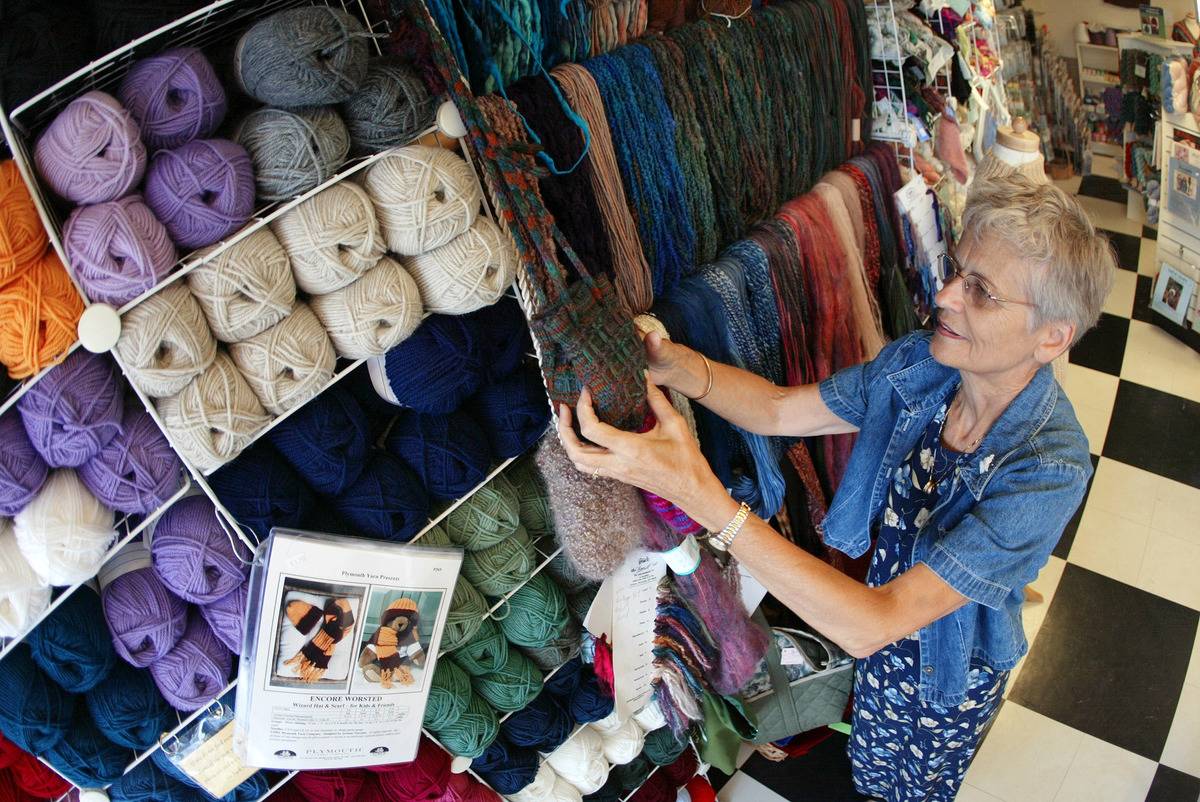 An elderly woman arranges yarn at a shop where she works.