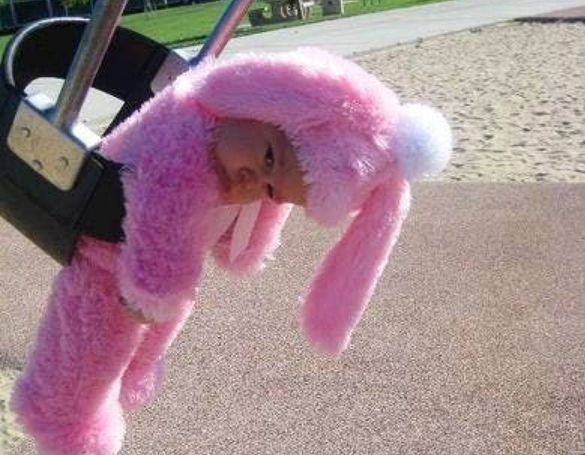 baby in bunny costume looking sad on swing at park