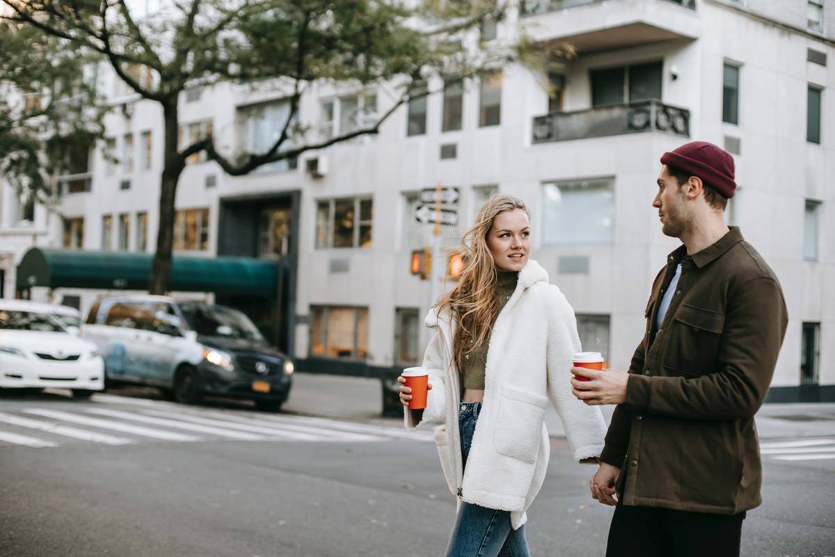 a guy and girl walking across the street holding coffee cups