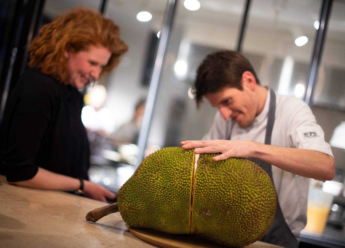 Two chefs cut a jackfruit open.