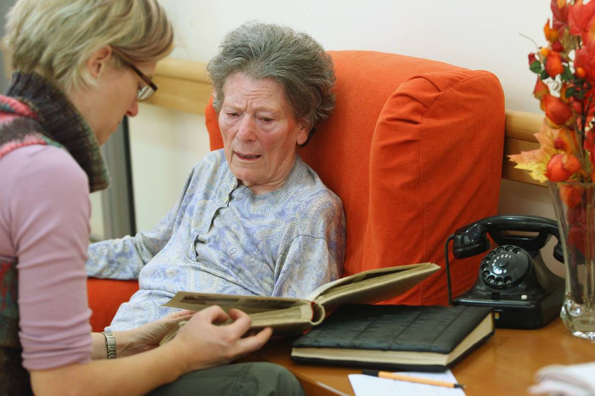 A therapist looks through a photo album with an elderly woman with dementia.