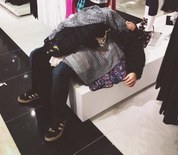 man lying down in a store with a bunch of clothes on him 