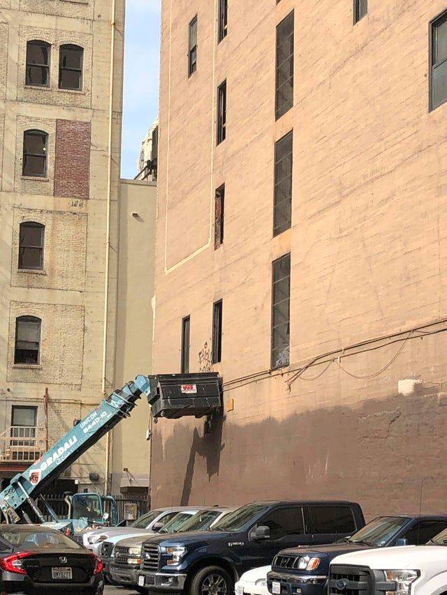 crane knocking dumpster into building over parked cars