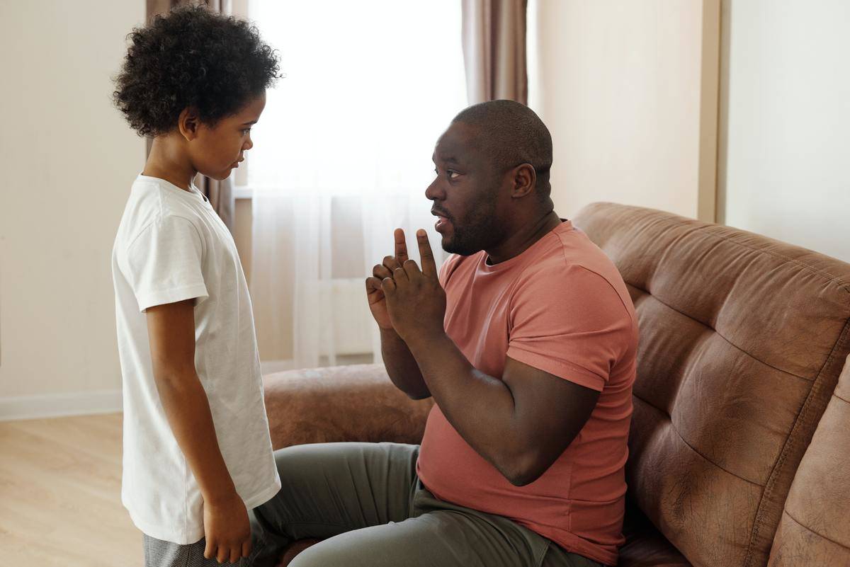 father speaking to child standing in front of him both looking serious