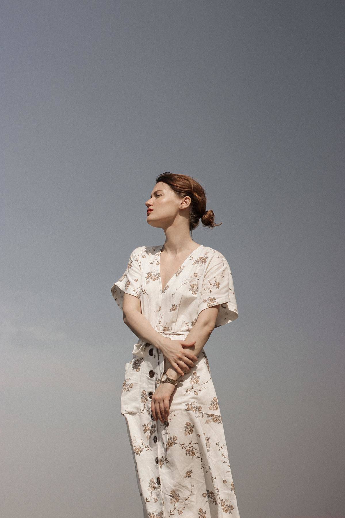 a woman wearing a floral dress looking up at a blue sky
