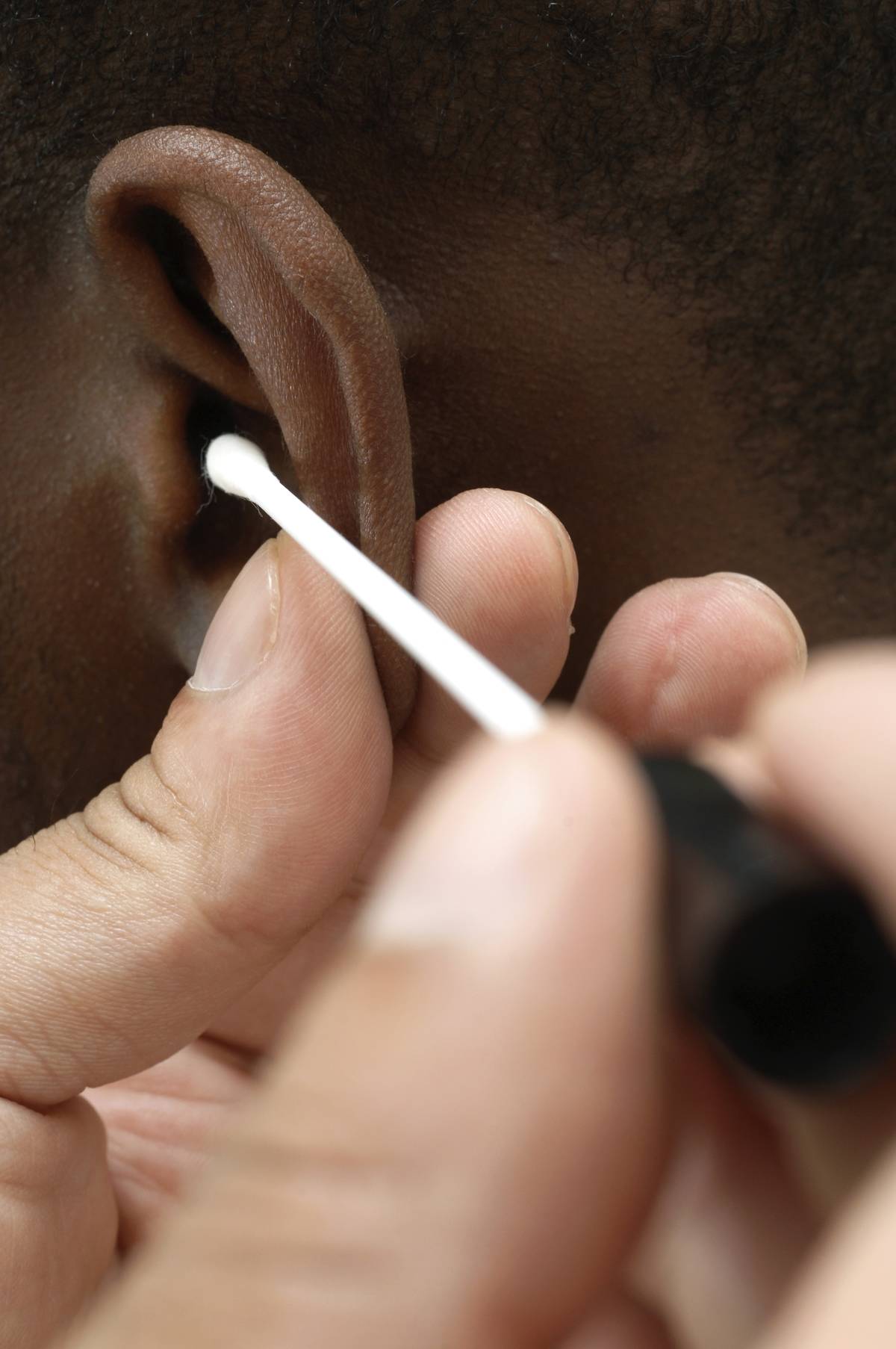 GP using cotton bud to clean ear canal of young male patient