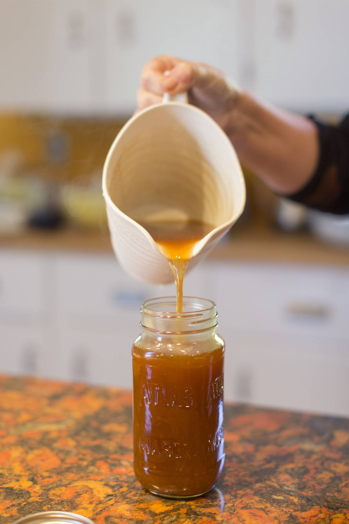 Christine Burns Rudalevige pours the finished vegetable broth made with raw vegetable and herb scraps into a mason jar