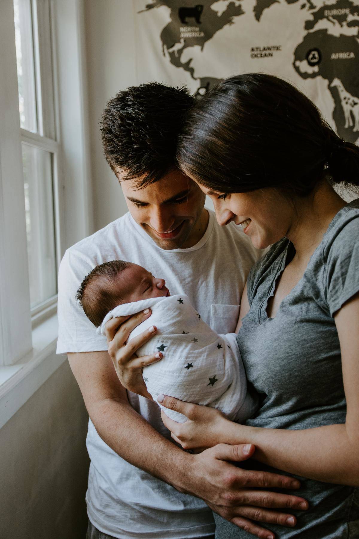 mom and dad holding a baby near a window 