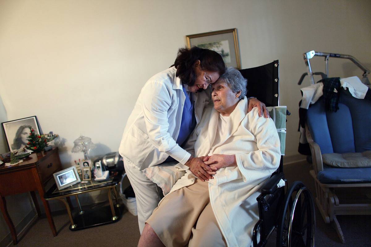 An elderly aid hugs a senior woman during home care.