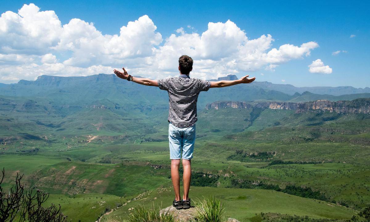 man standing on cliff looking out over valley