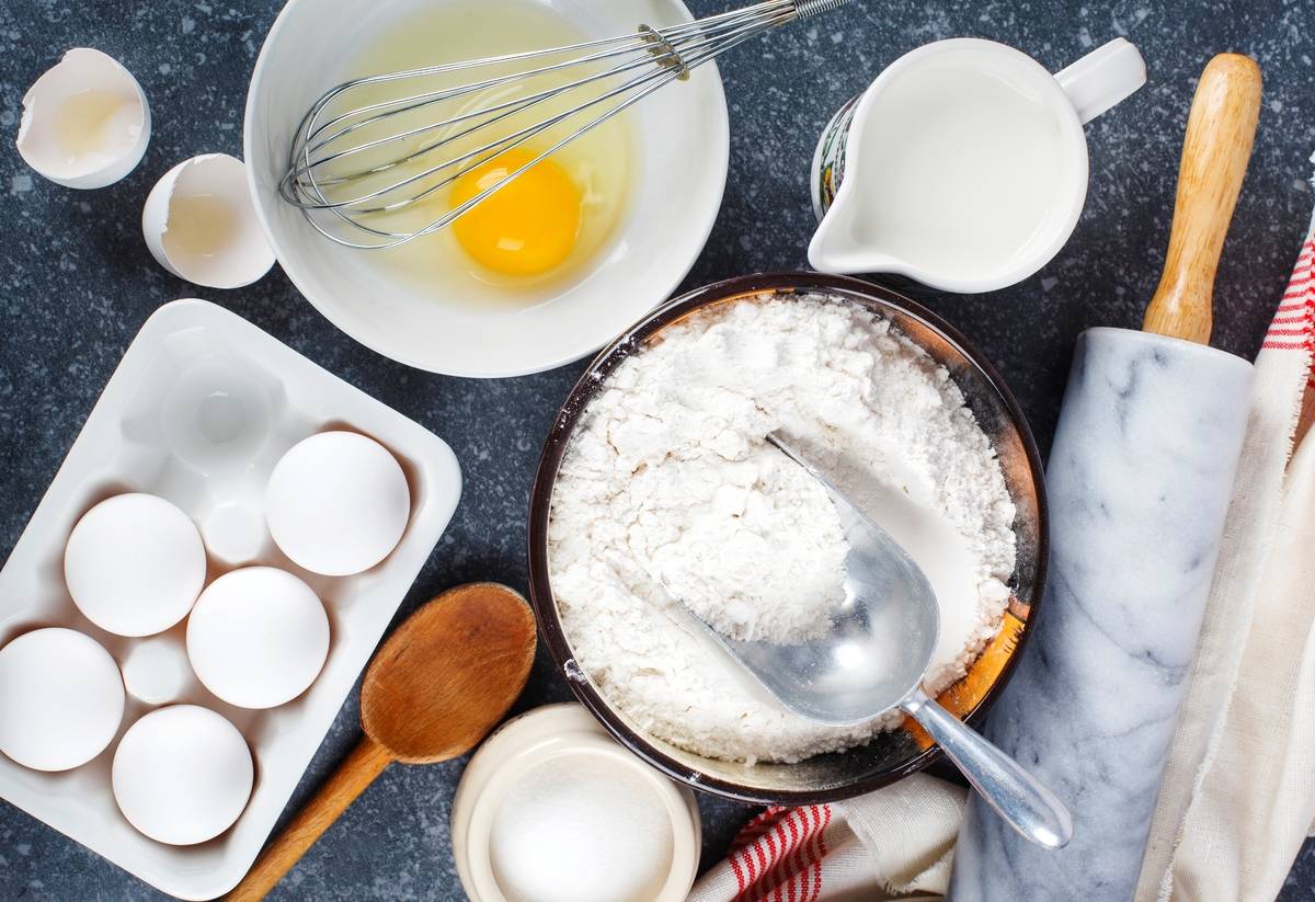 Marble rolling pin with flour, milk, sugar and eggs on a dark background. Top view