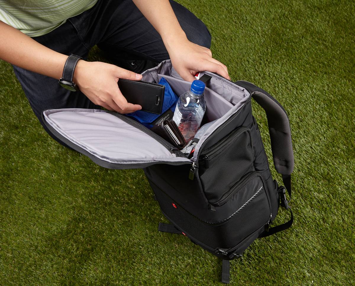 A man packs a water bottle, phone, and wallet into his backpack.