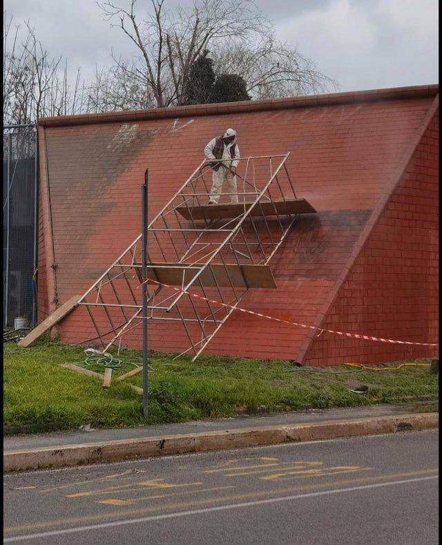 man standing on toppled scaffolding to paint wall