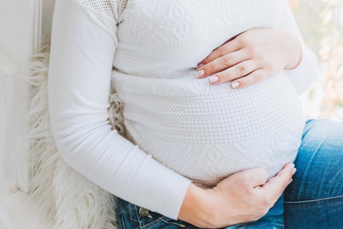pregnant woman in white knit sweatershirt holding belly