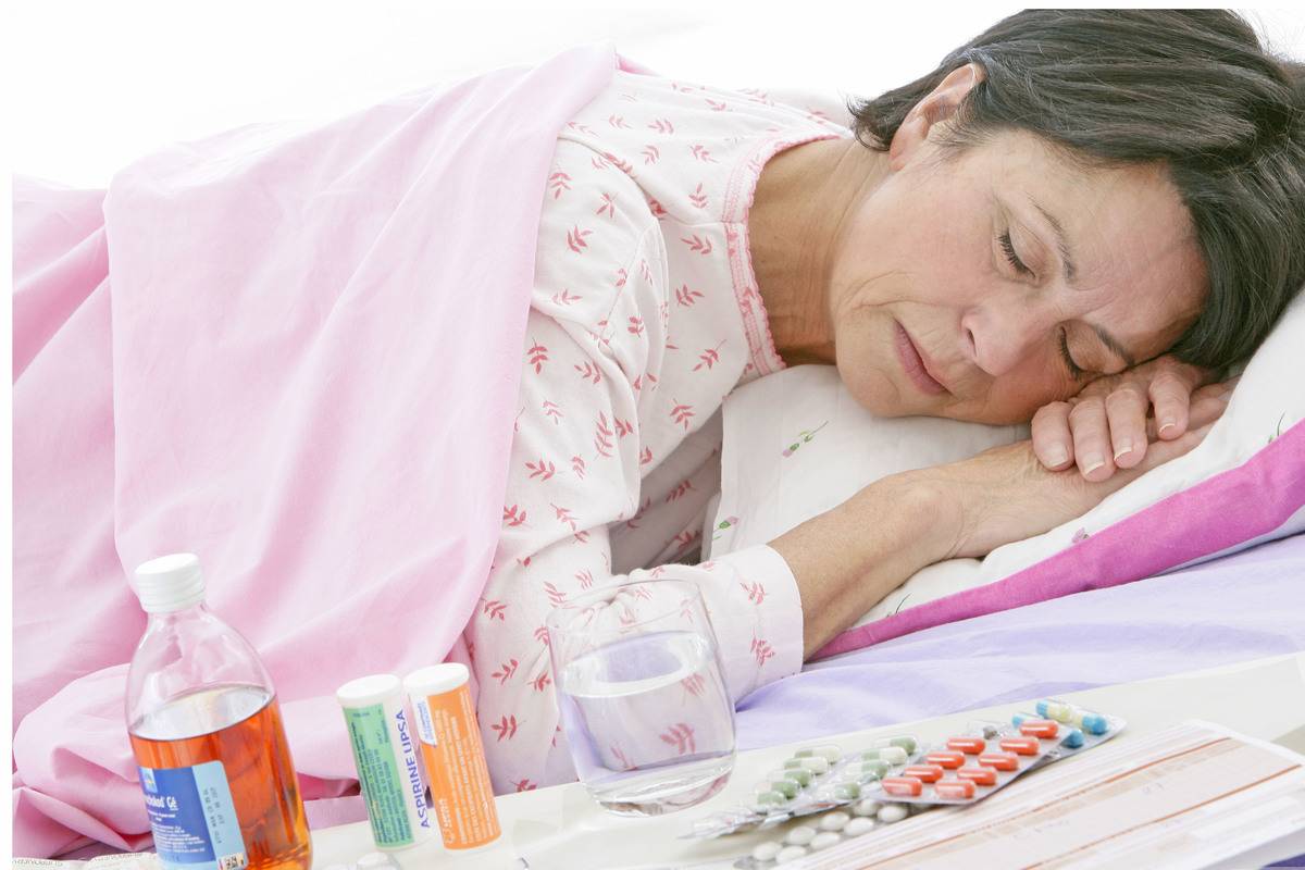 An elderly woman sleeps next to medications on the table.