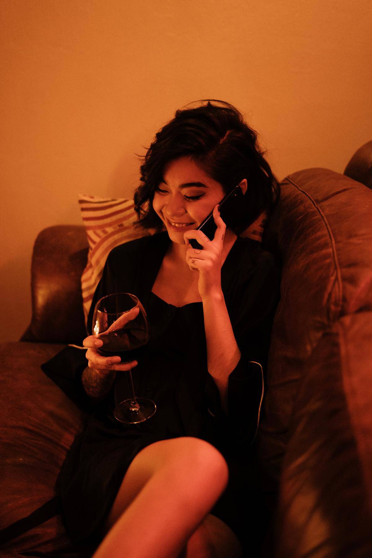 a woman holding wine in one hand while talking on the phone