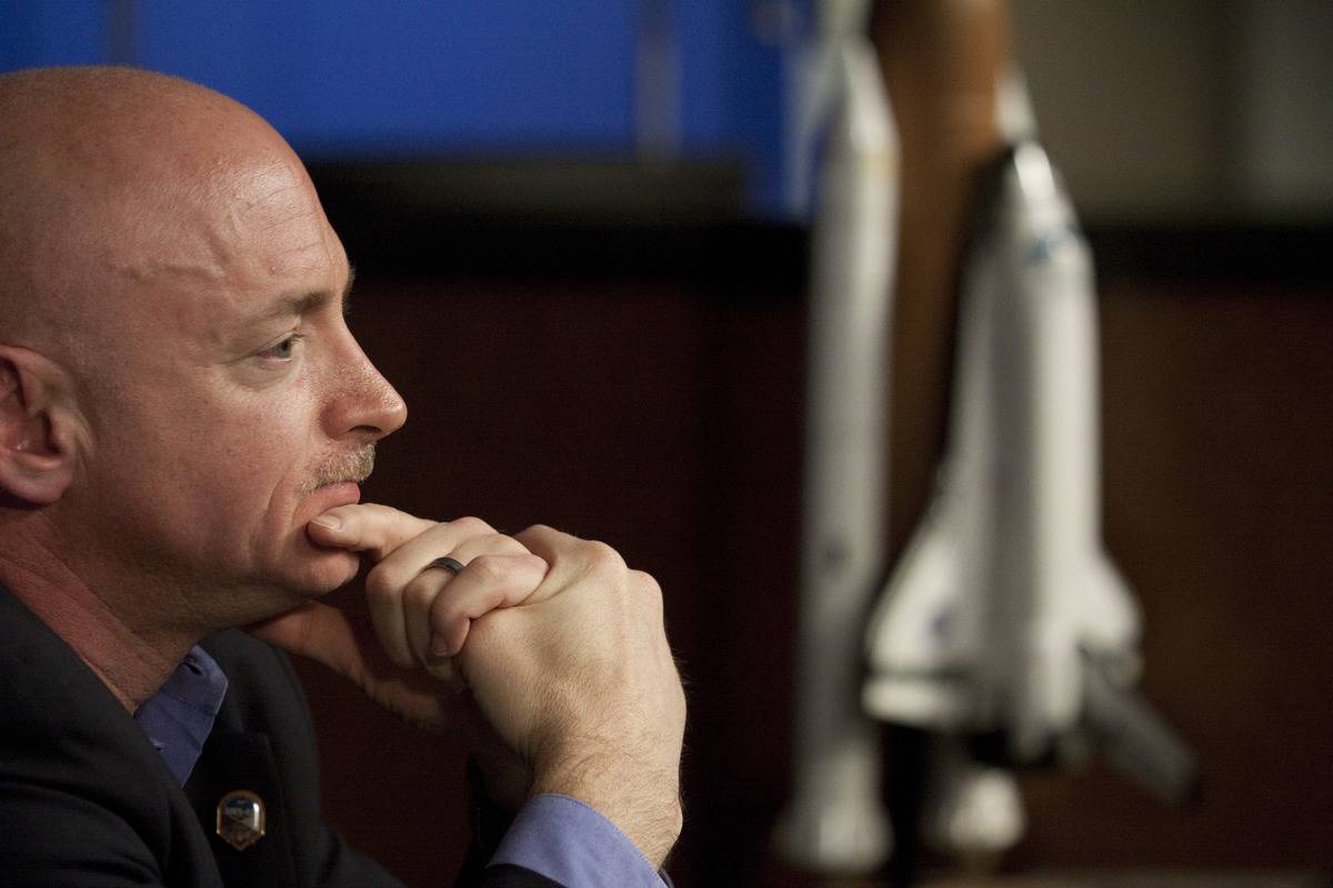 Mark Kelly sits and ponders next to a statue of a rocket.