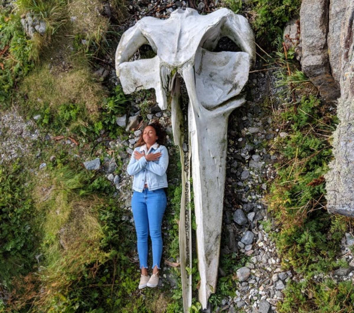woman laying down with her arms crossed over her chest next to a massive whale skull