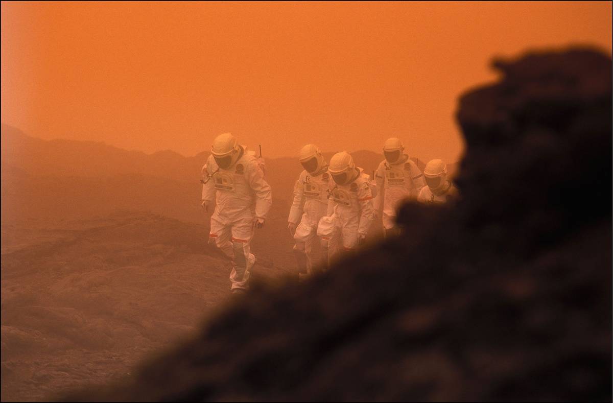 Five men and women walk along Mars in a storm.