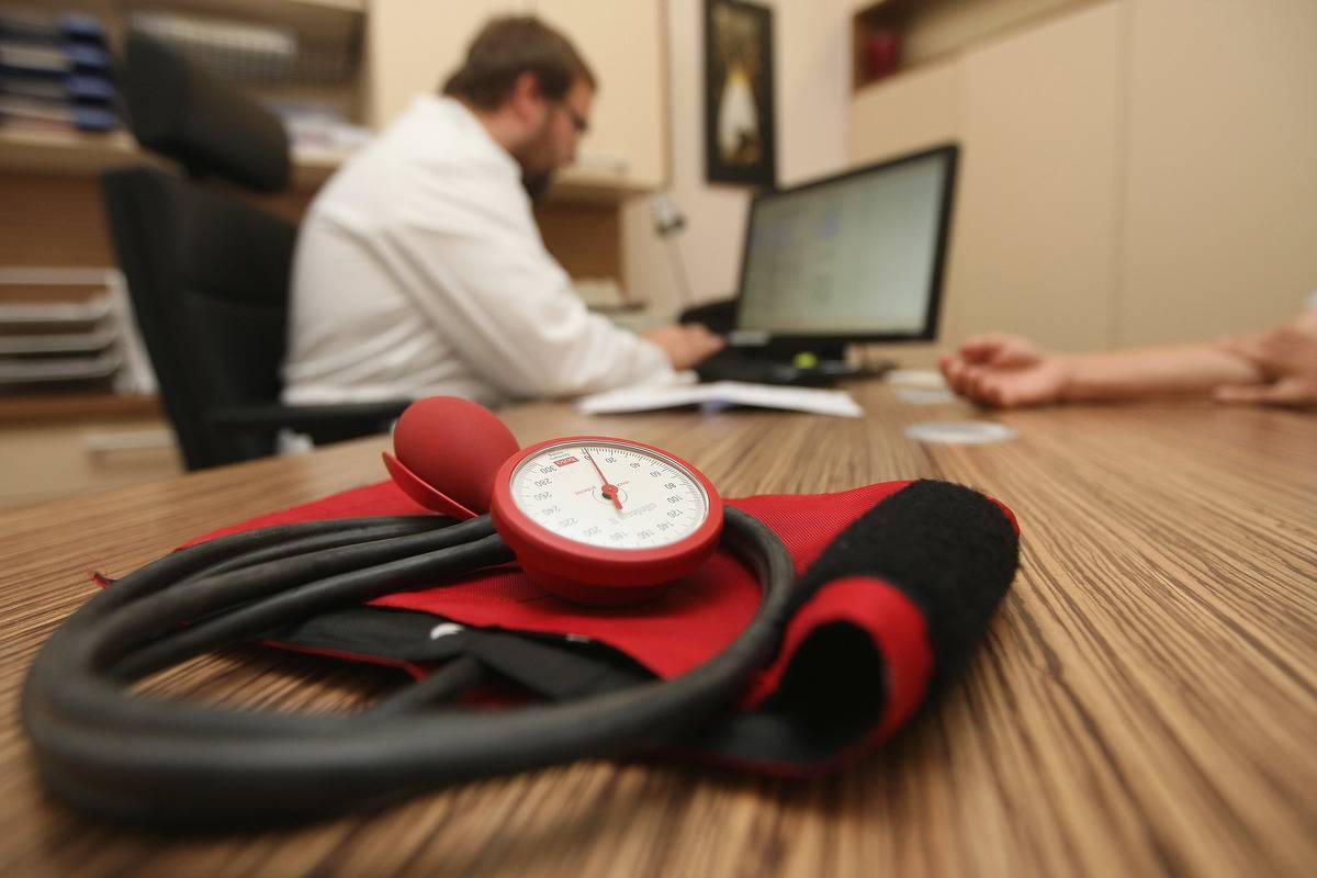 A doctor speaks to a patient as a sphygmomanometer, or blood pressure meter, lies on his desk.
