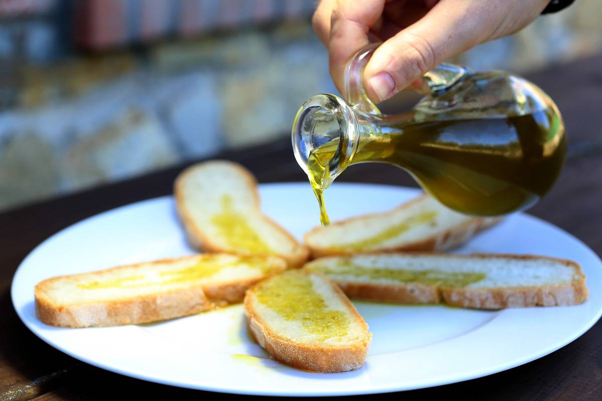 A person pours olive oil on bread.