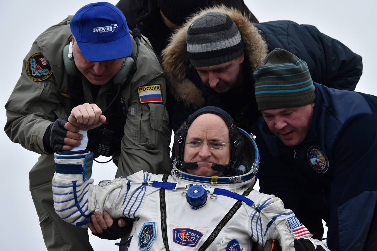 Three men help Scott Kelly get out of a space capsule.