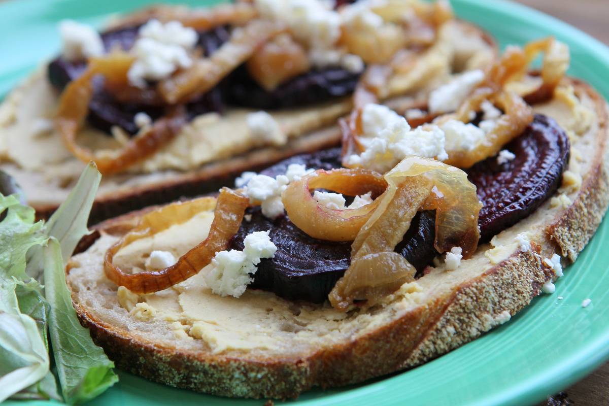 A sandwich includes hummus, roasted onions, beets, and feta.