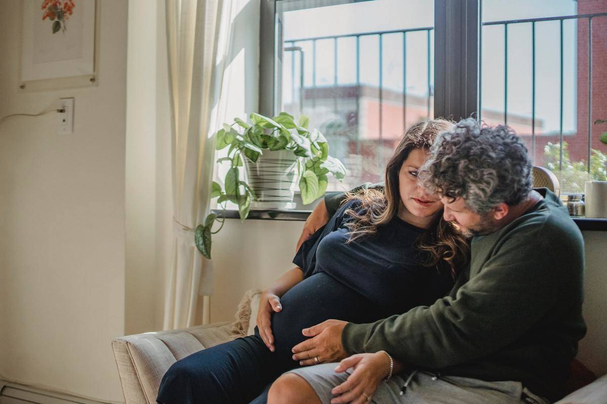 man holds pregnant belly while they sit