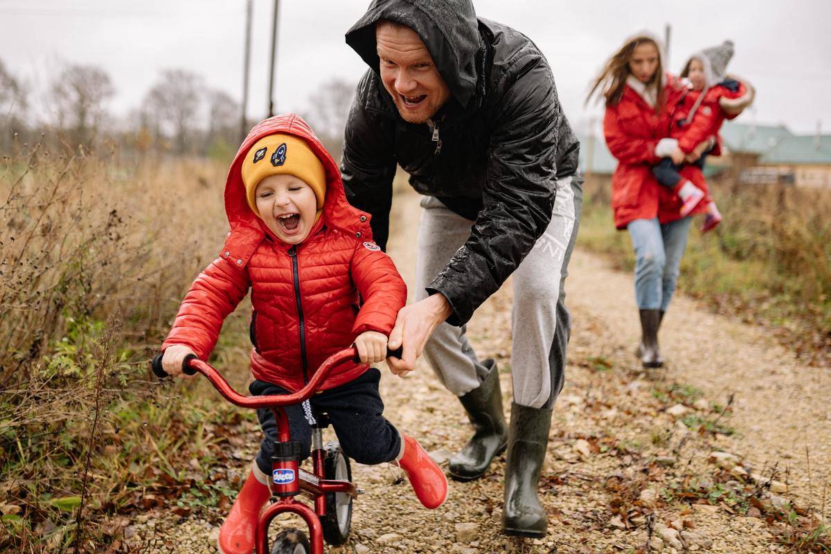 man pushing laughing child in red coat on bike