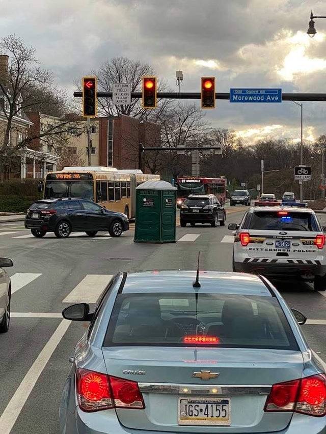 port-o-potty at intersection surrounded by cars