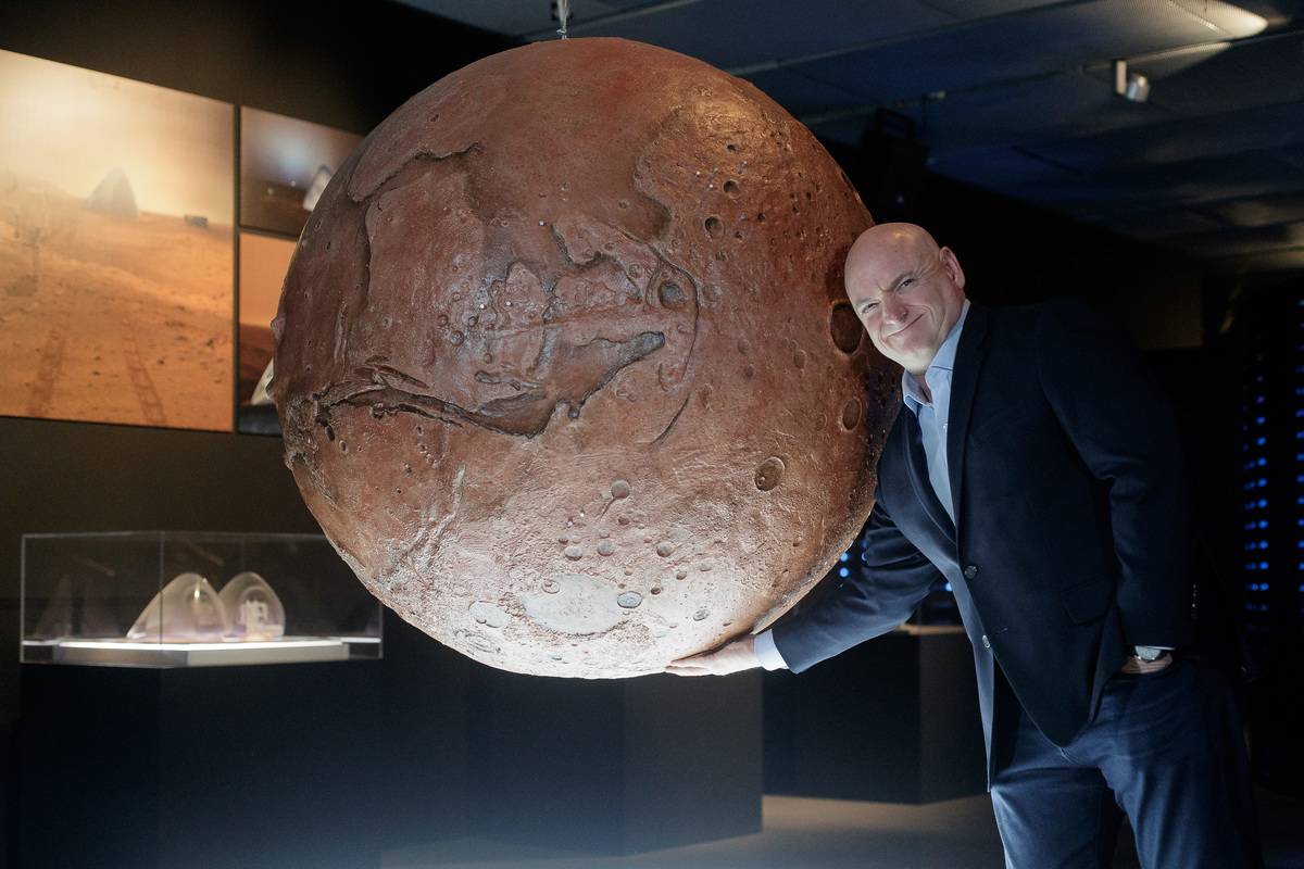 Scott Kelly stands next to a model of the planet Mars.