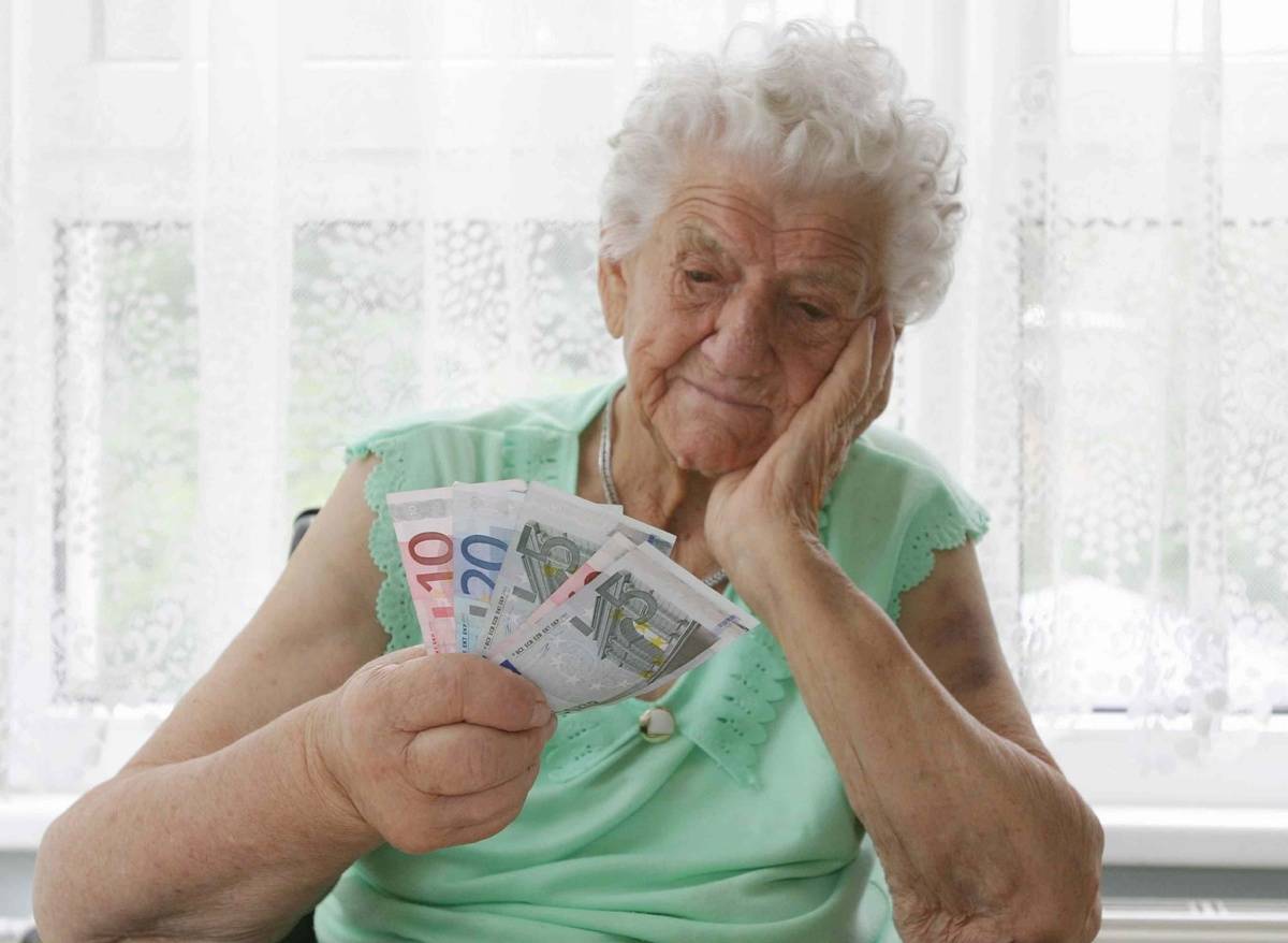 An elderly women stars that the Euros she holds.