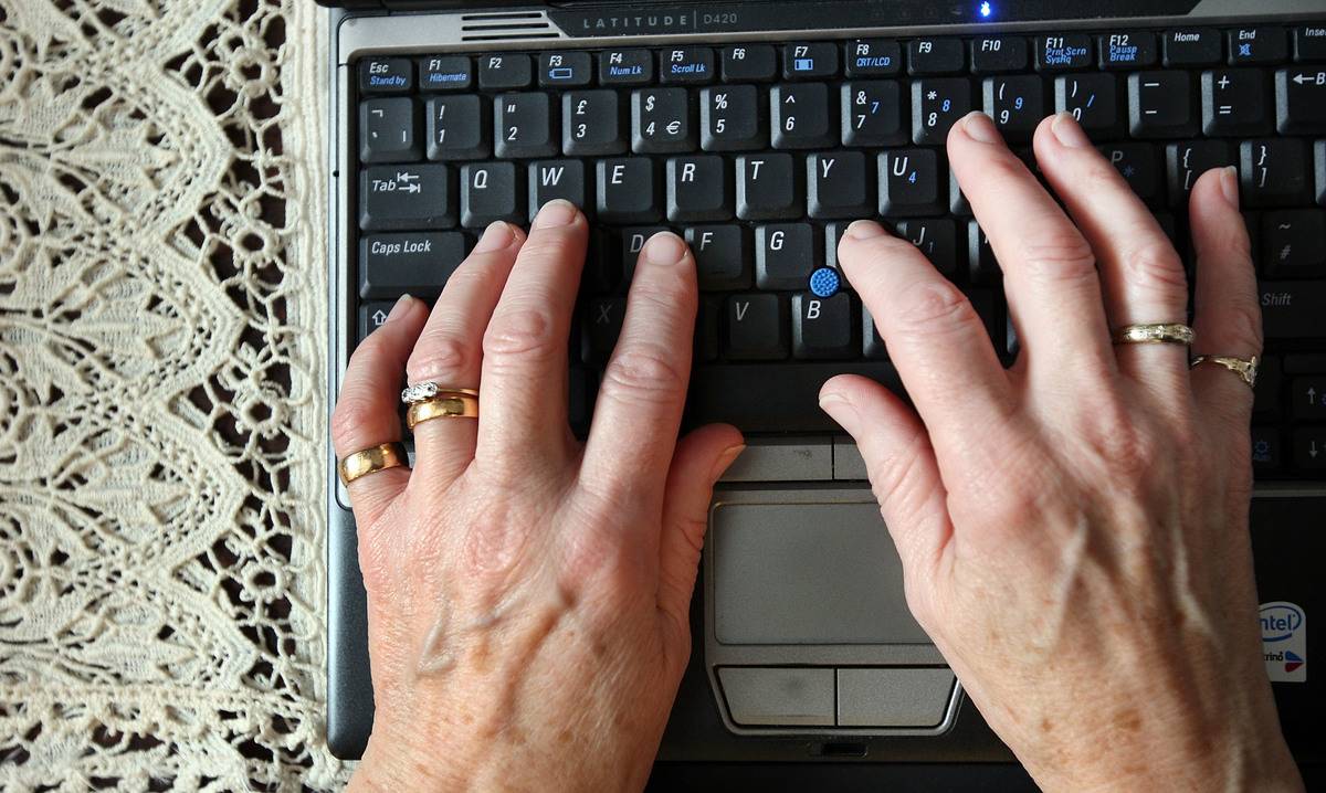 An elderly woman types on a laptop.