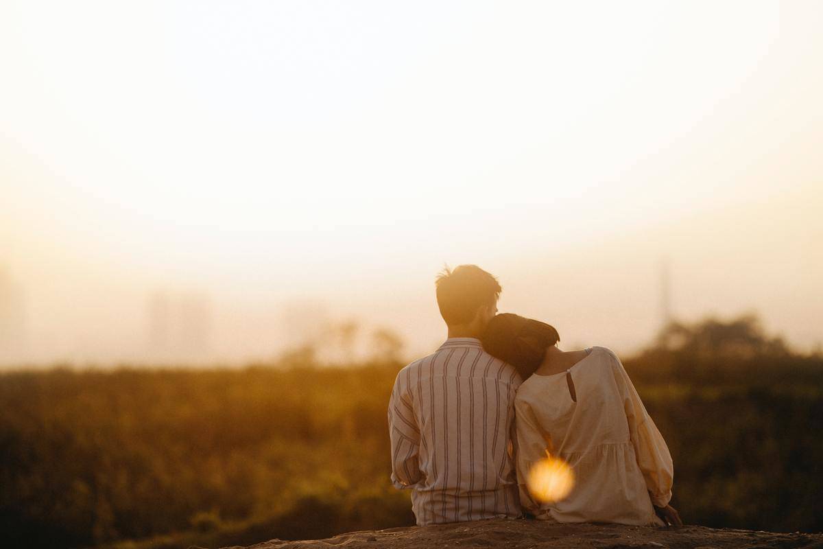 woman leans on man's shoulder in the sunset