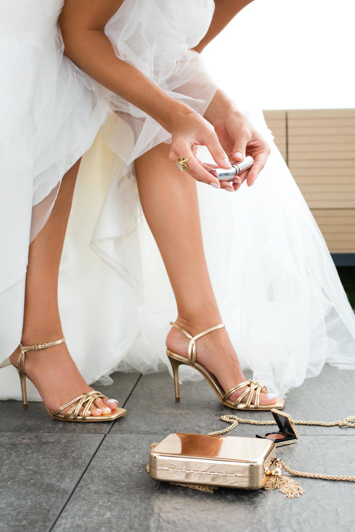 Bride's legs, shoes, clutch on ground, blush open on ground, looks like contents spilled out of her bag.