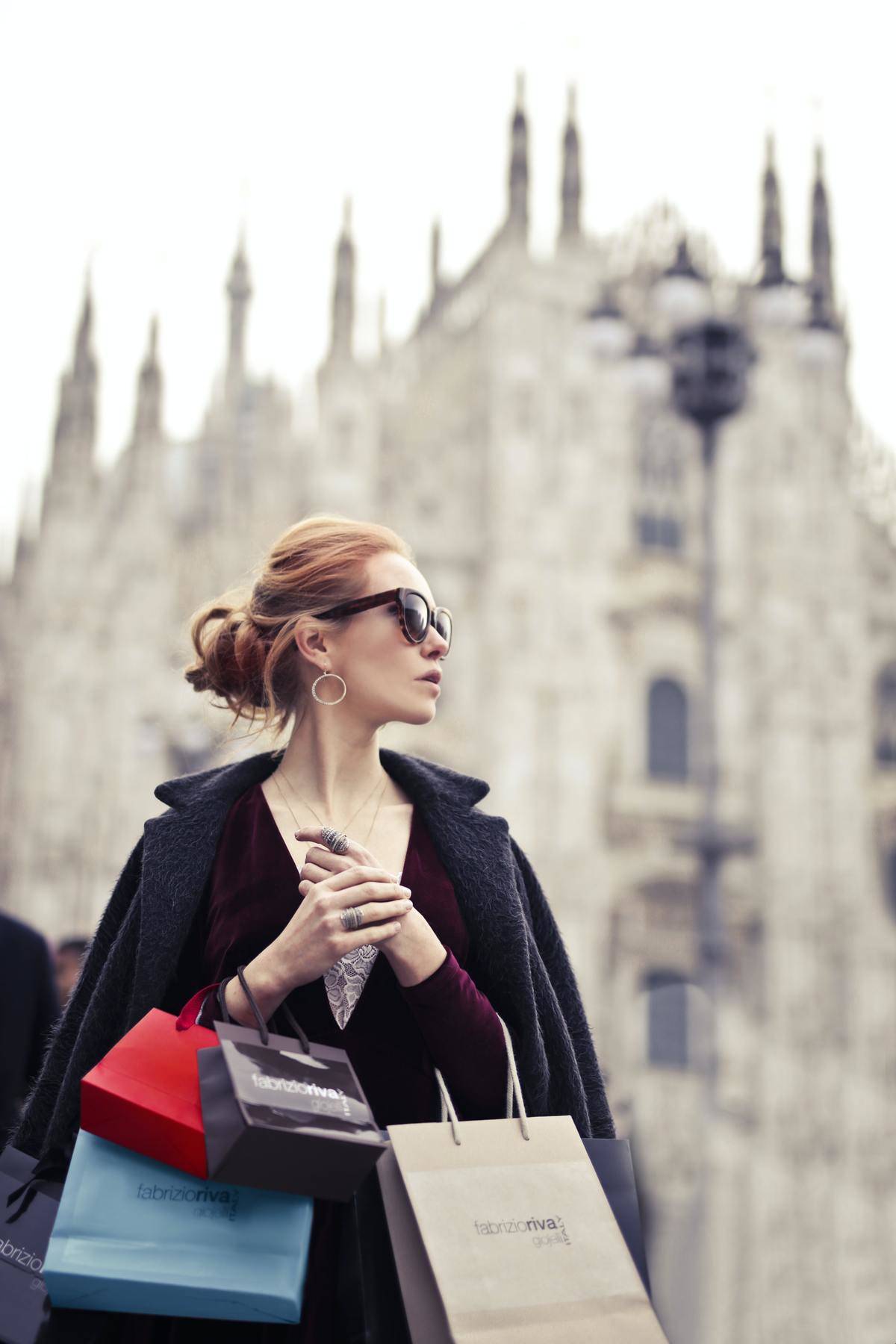 Classy woman wearing peacoat, jewellery and sunglasses carrying multiple high fashion brand shopping bags