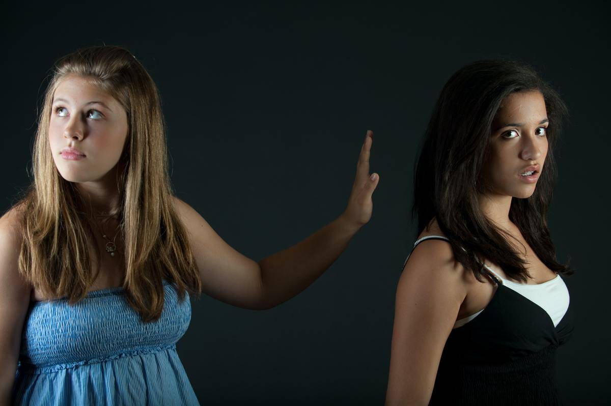 Girl in blue shirt holds hand out and looks away from teen girl in black and white tank top