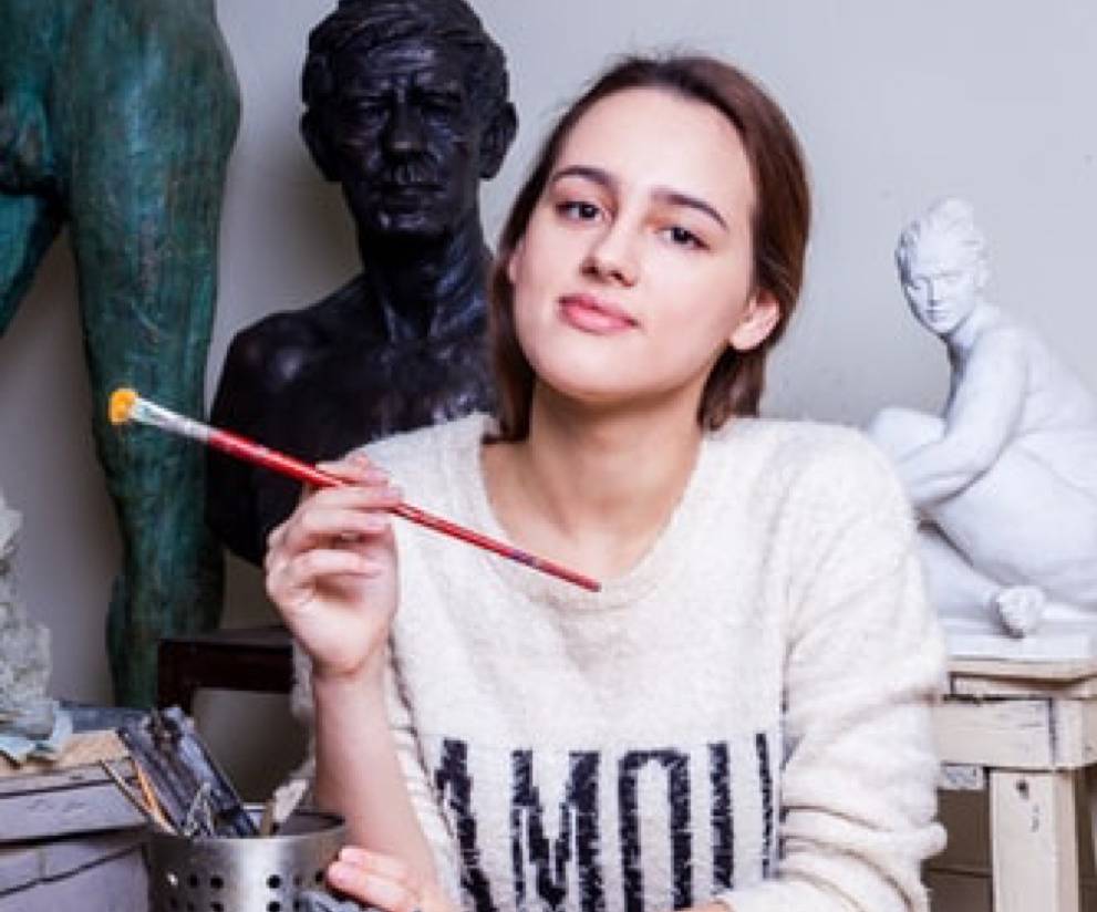 woman holding paint brush and staring ahead with statues in the background