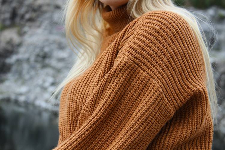 Torso of a blonde woman in an orange turtleneck sweater