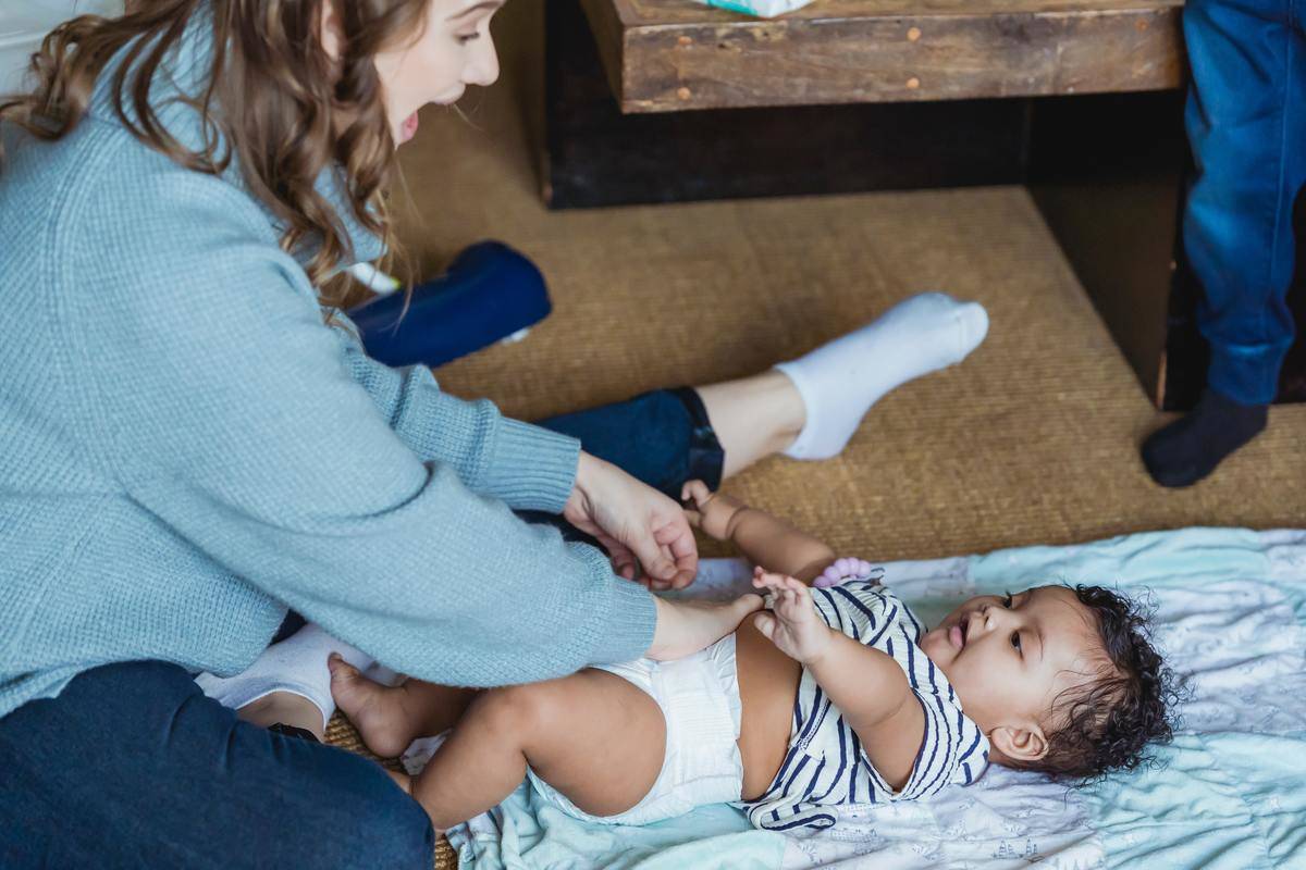 woman laughing at baby on floor while changing diaper